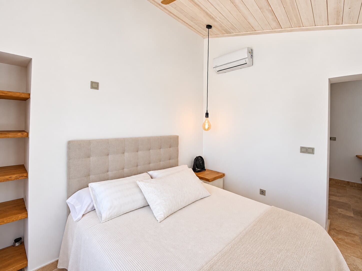Dormitorio luminoso con techo de vigas blancas y cama de lino